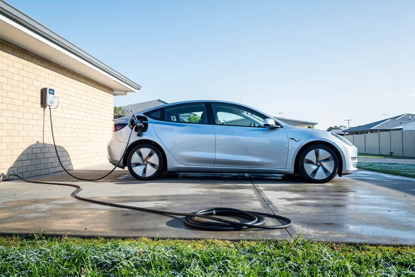 A split graphic showing a single phase home EV charger plugged into a wallbox, with two power readouts side by side, 4.6kW and 7.4kW, against a Queensland suburban driveway at night.